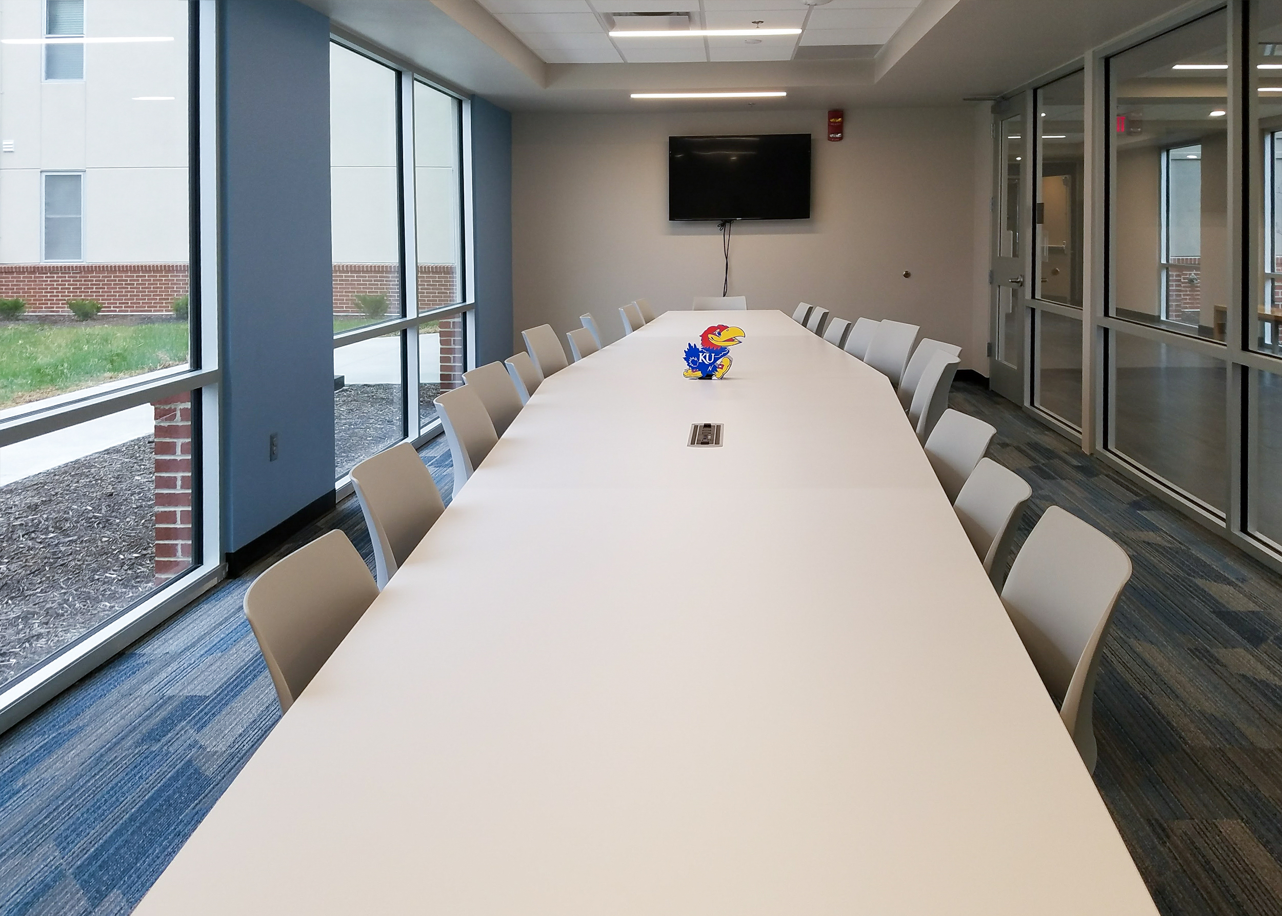 A conference table, next to a window, surrounded by office chairs on two sides.