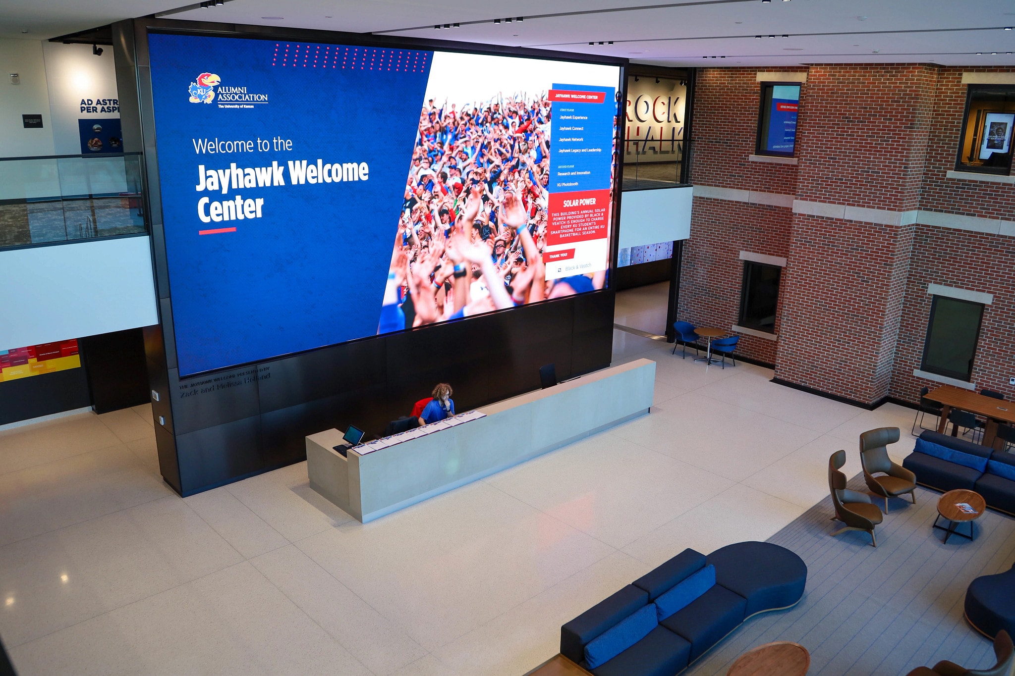 A two-story screen displays greeting messages to visitors in the lobby of the Jayhawk Welcome Center.
