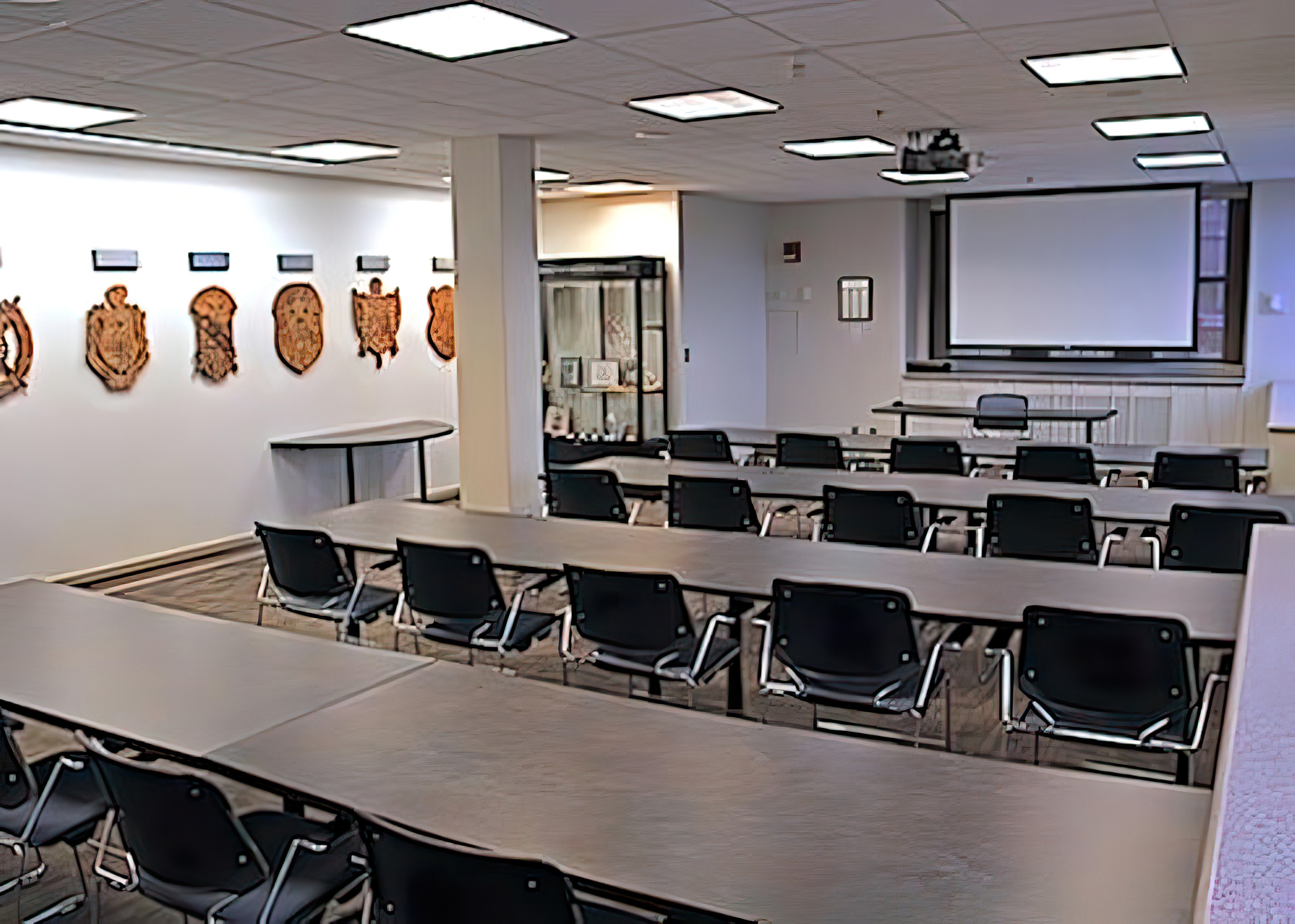 Tables and chairs arranged in rows face a dropdown view-screen. The crests of historically black sororities and fraternities adorn the walls.