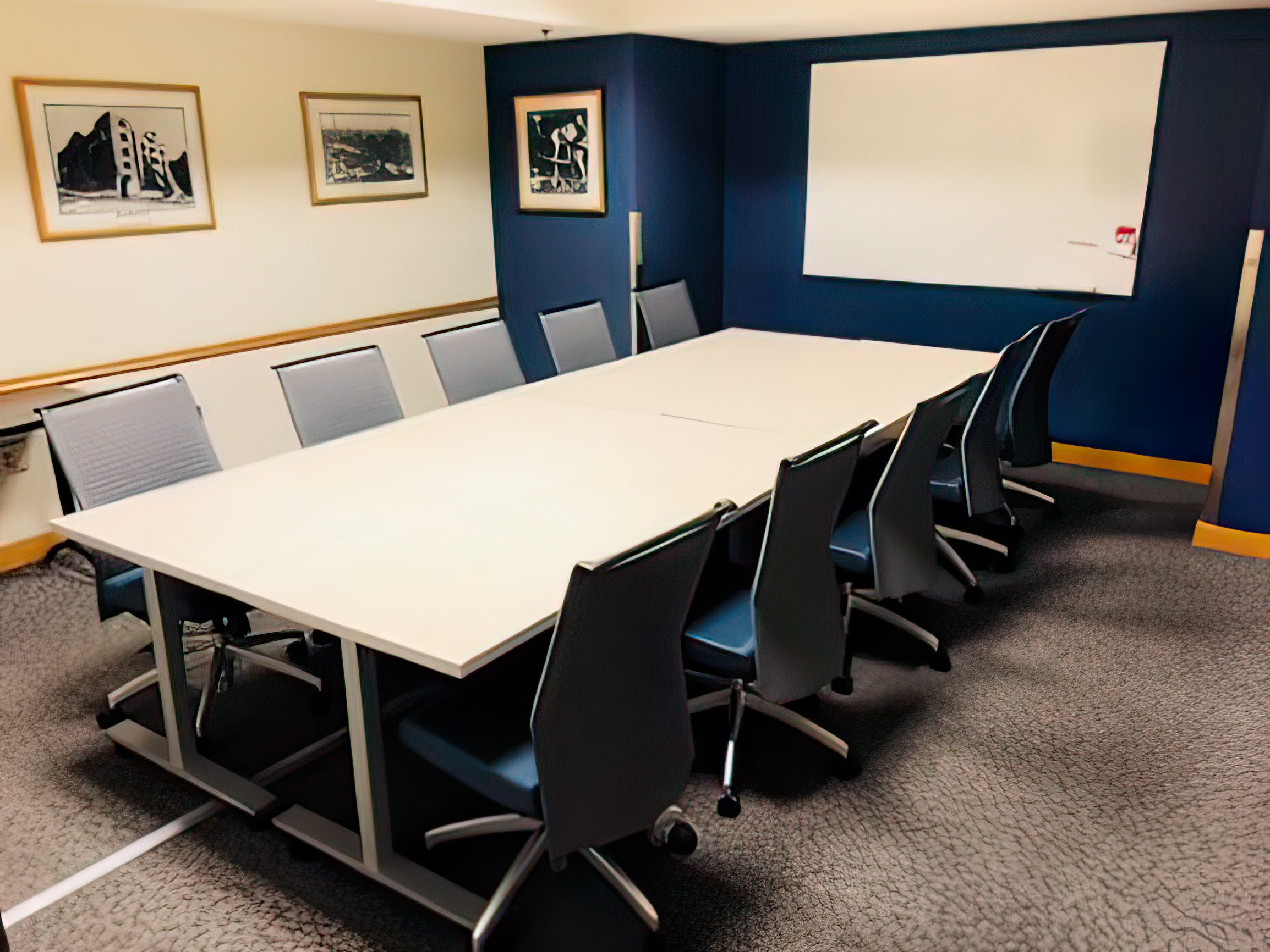 A conference table, with chairs on two sides, faces a blue wall with a whiteboard.