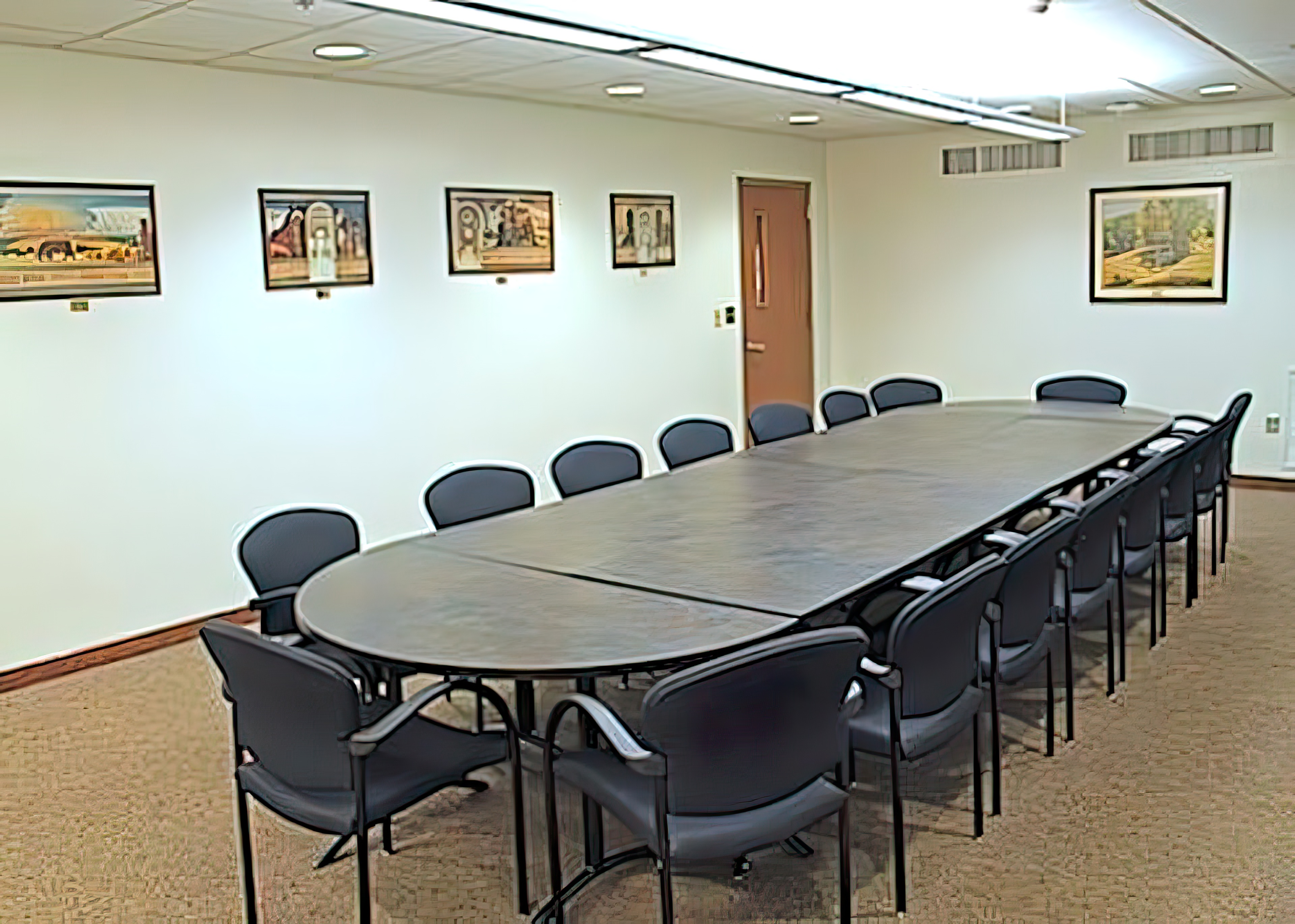 Chairs surround a large, pill-shaped table. Small paintings adorn the walls.