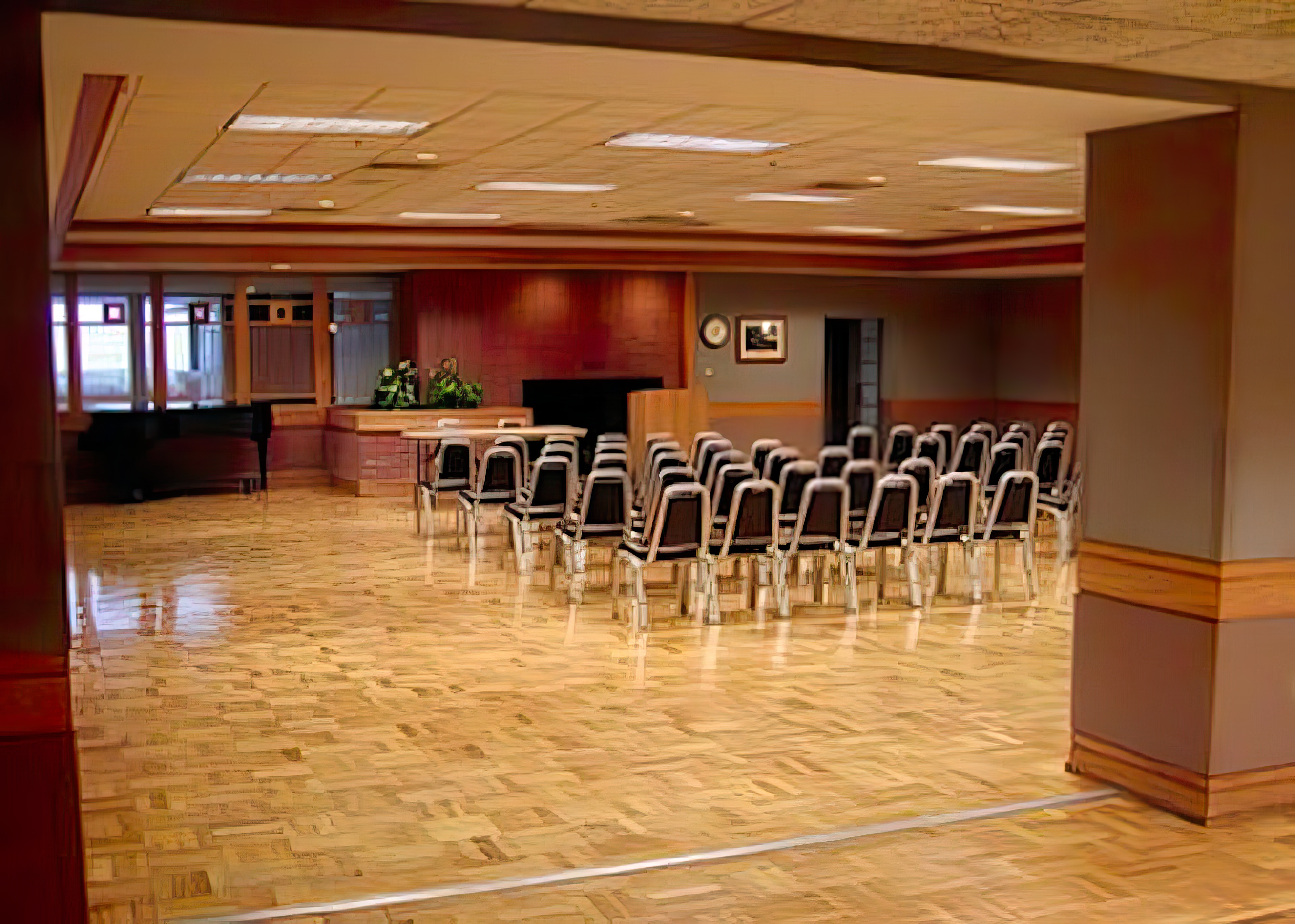 A spacious room with glossy parquet flooring. Rows of chairs face a speakers podium.