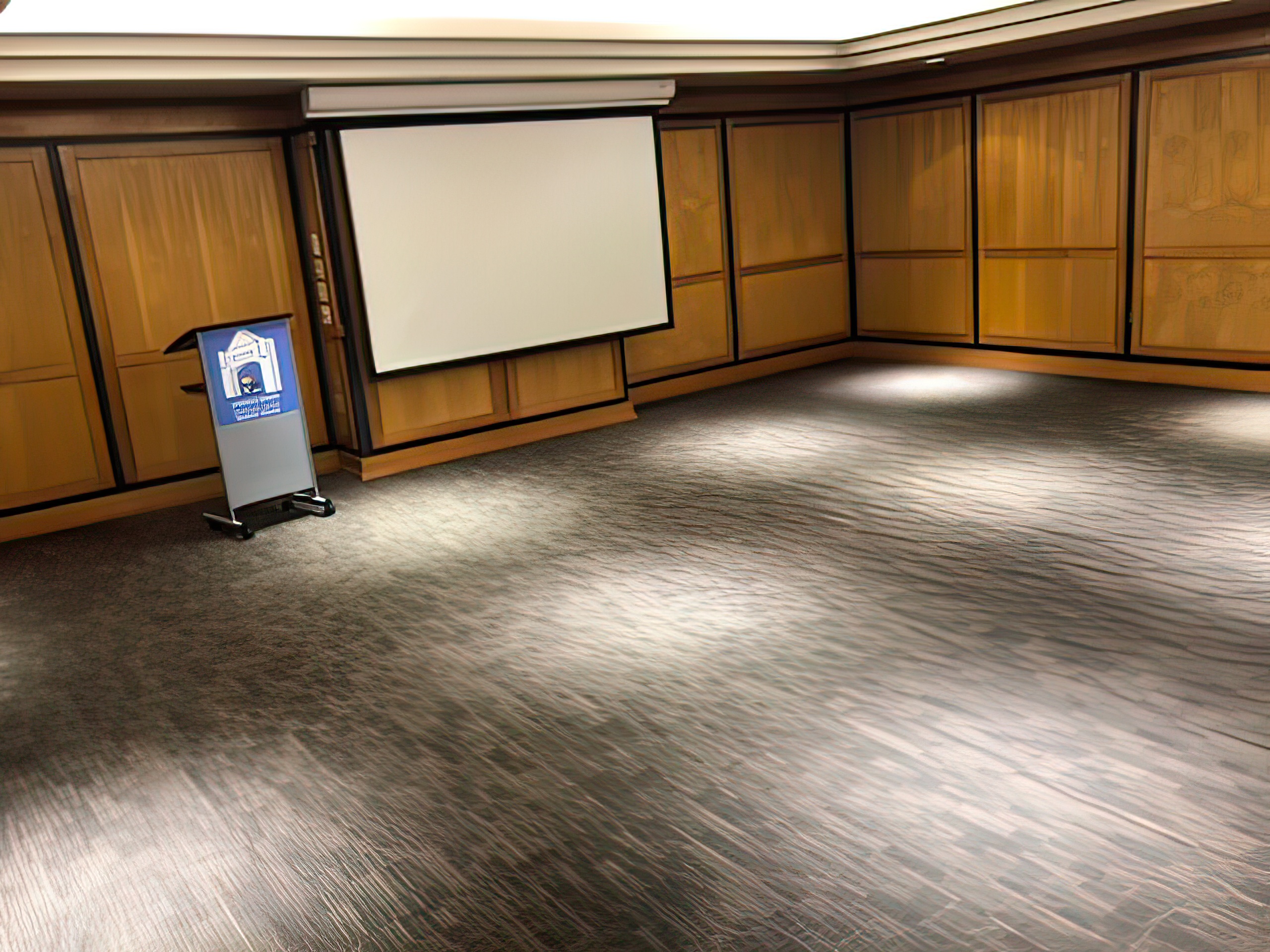 A speaker's podium and dropdown view-screen before an open room.