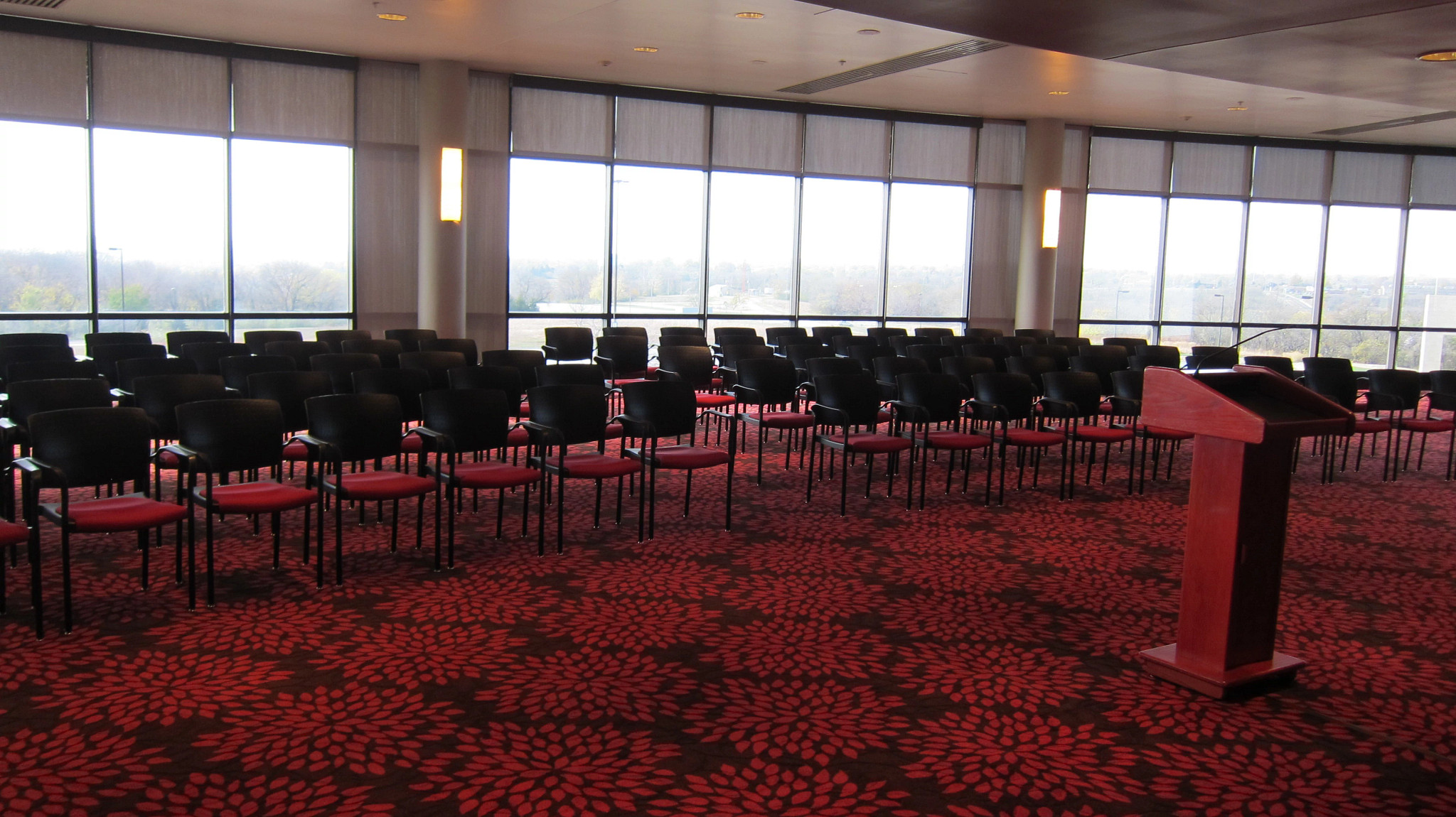 Chairs lined up in rows facing a podium in a large room with a curved wall of windows in the background.