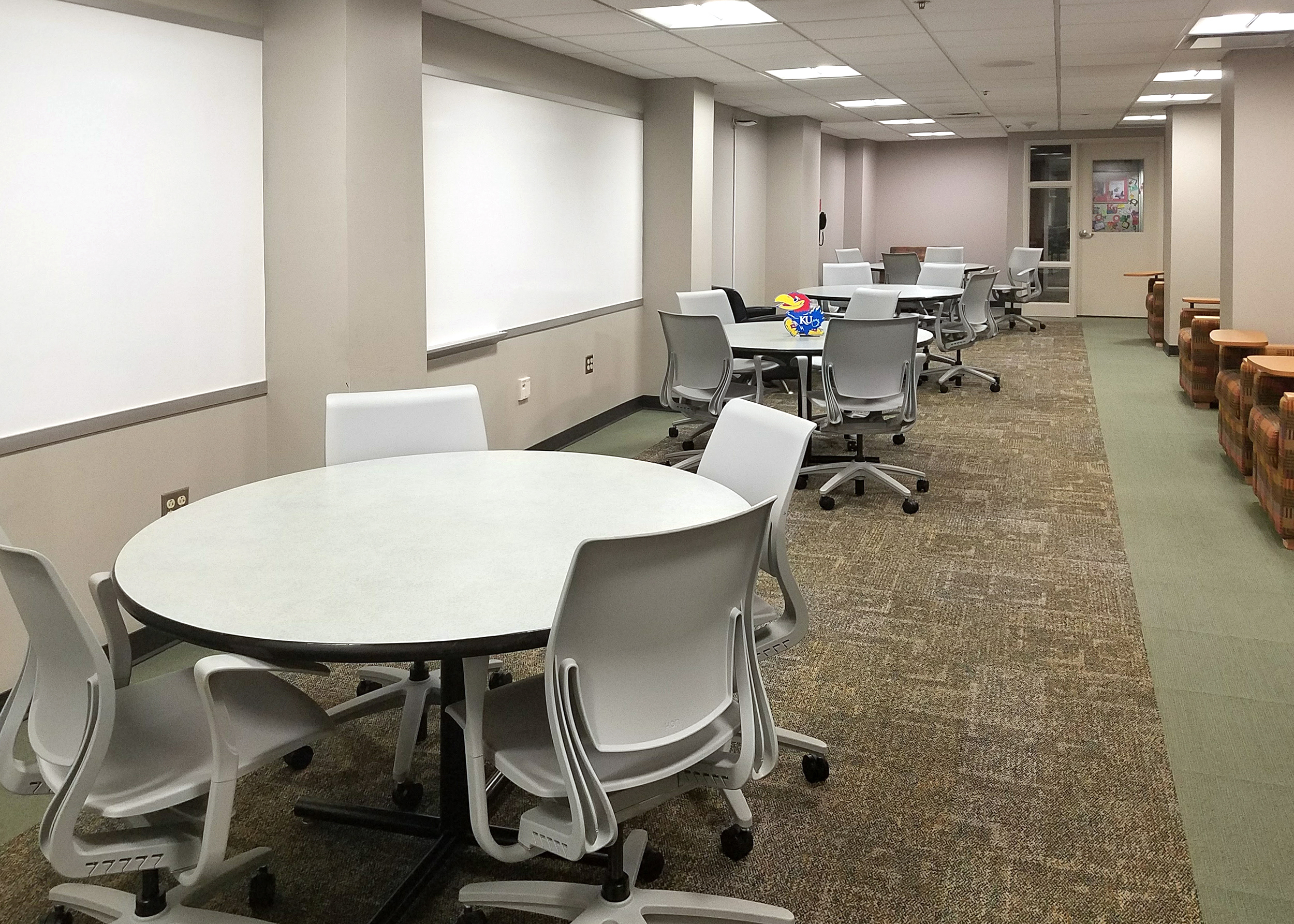 A large room with several round tables and chairs positioned in front of white boards.